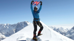 Person standing on top of a snowy mountaintop holding a UK flag